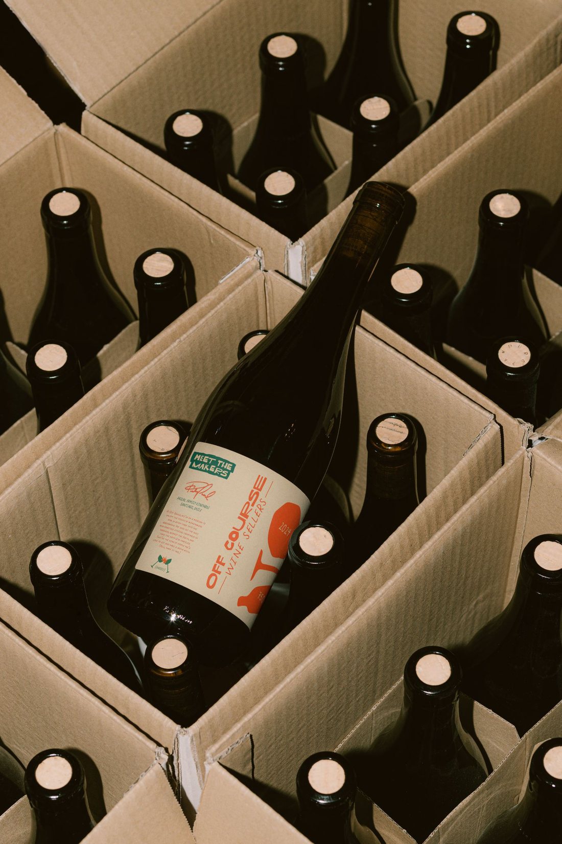 A hand pulling an Off Course bottle from a branded box